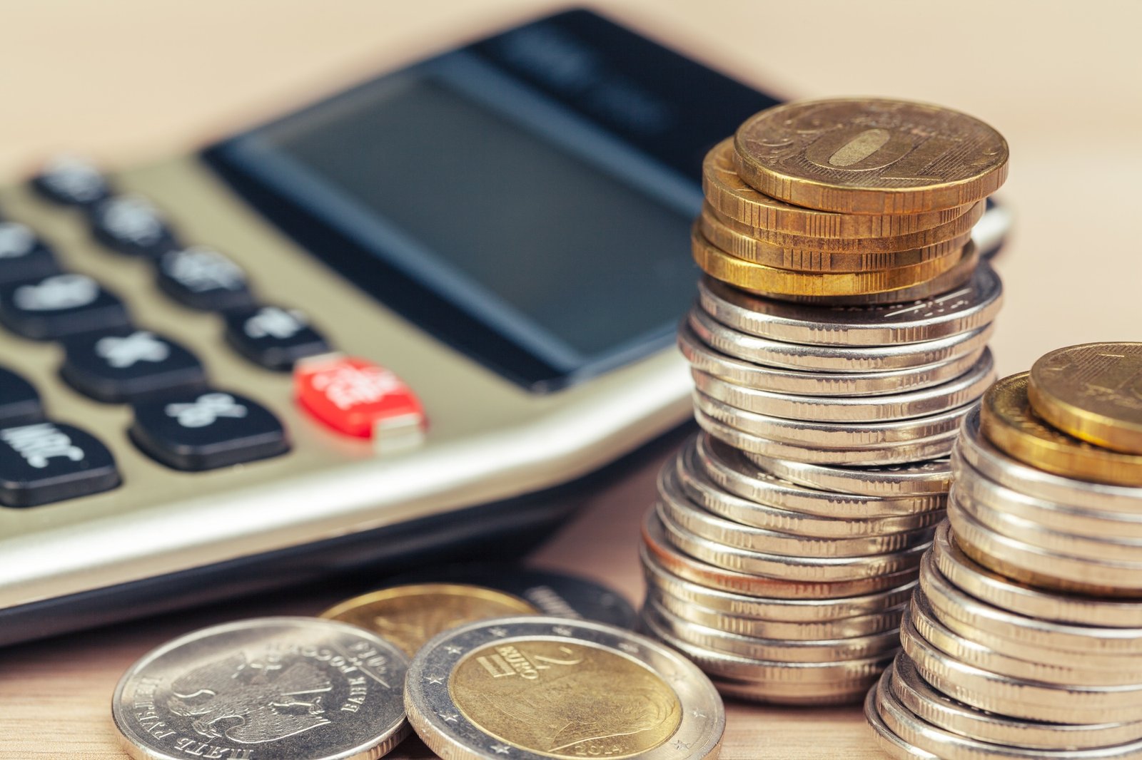 Montones de monedas junto a una calculadora sobre una superficie de madera.